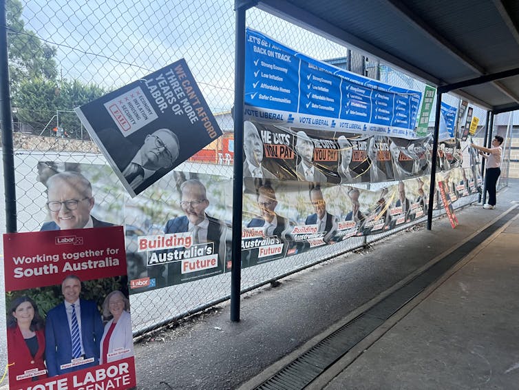 Reams of lightweight plastic posters adorn a tennis court on the way into the polling booth at Magill School, with a person taking down posters.