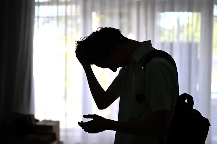 Silhouette of an anguished young man with his head in his hands.
