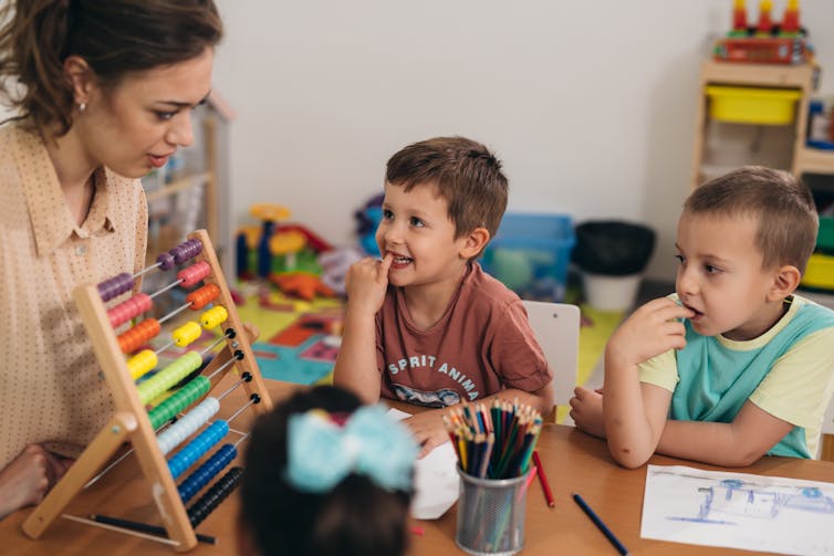 Two children sitting with a woman and abacus