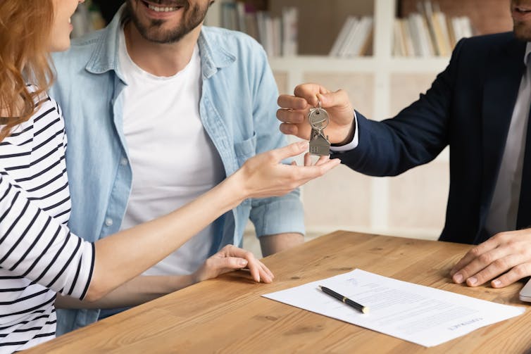 Man in suit handing keys to a woman and man