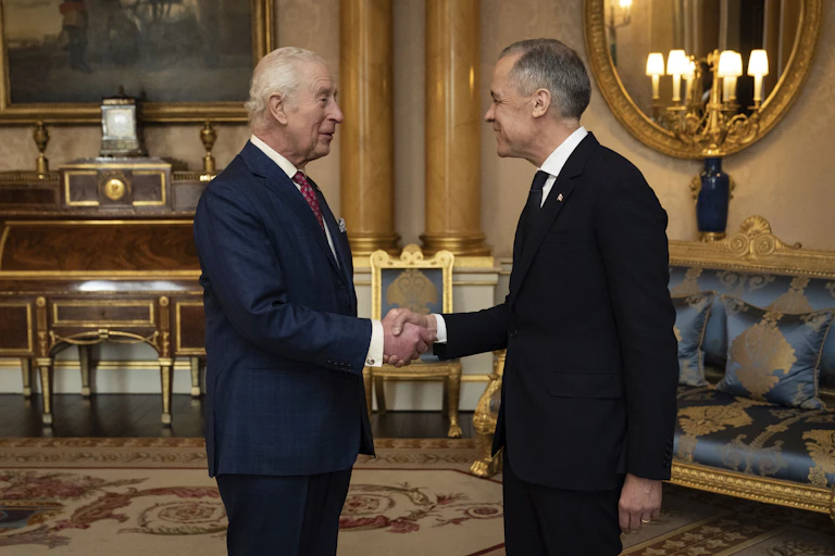 Two men, one elderly, shake hands and smile in an ornate sitting room.