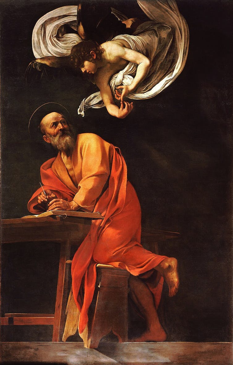 A bearded man in a saffron robe writing at his desk, with an angel hovering above him.