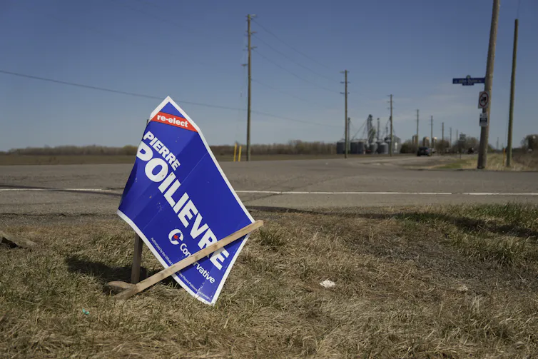 A crumpled Pierre Poilievre sign by the side of a road.