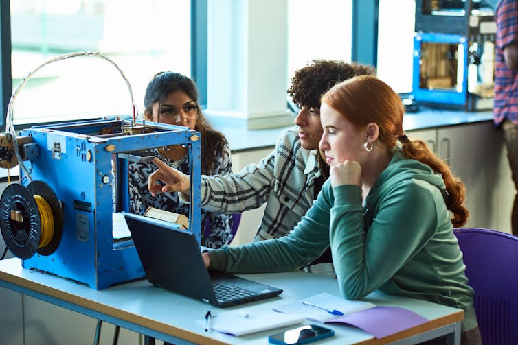 Three college students sit at a desk using a laptop for a project.
