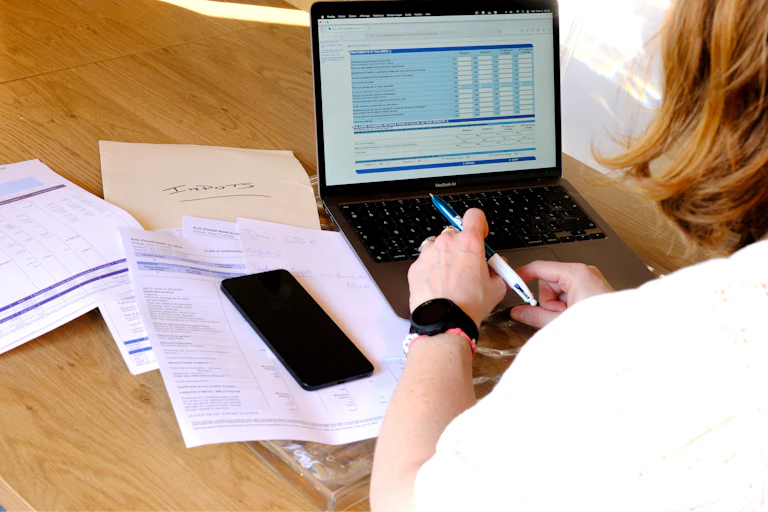 A woman looks over a stack of papers at her computer screen