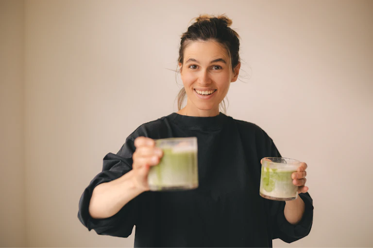 Smiling woman holds a glass of matcha tea in each hand