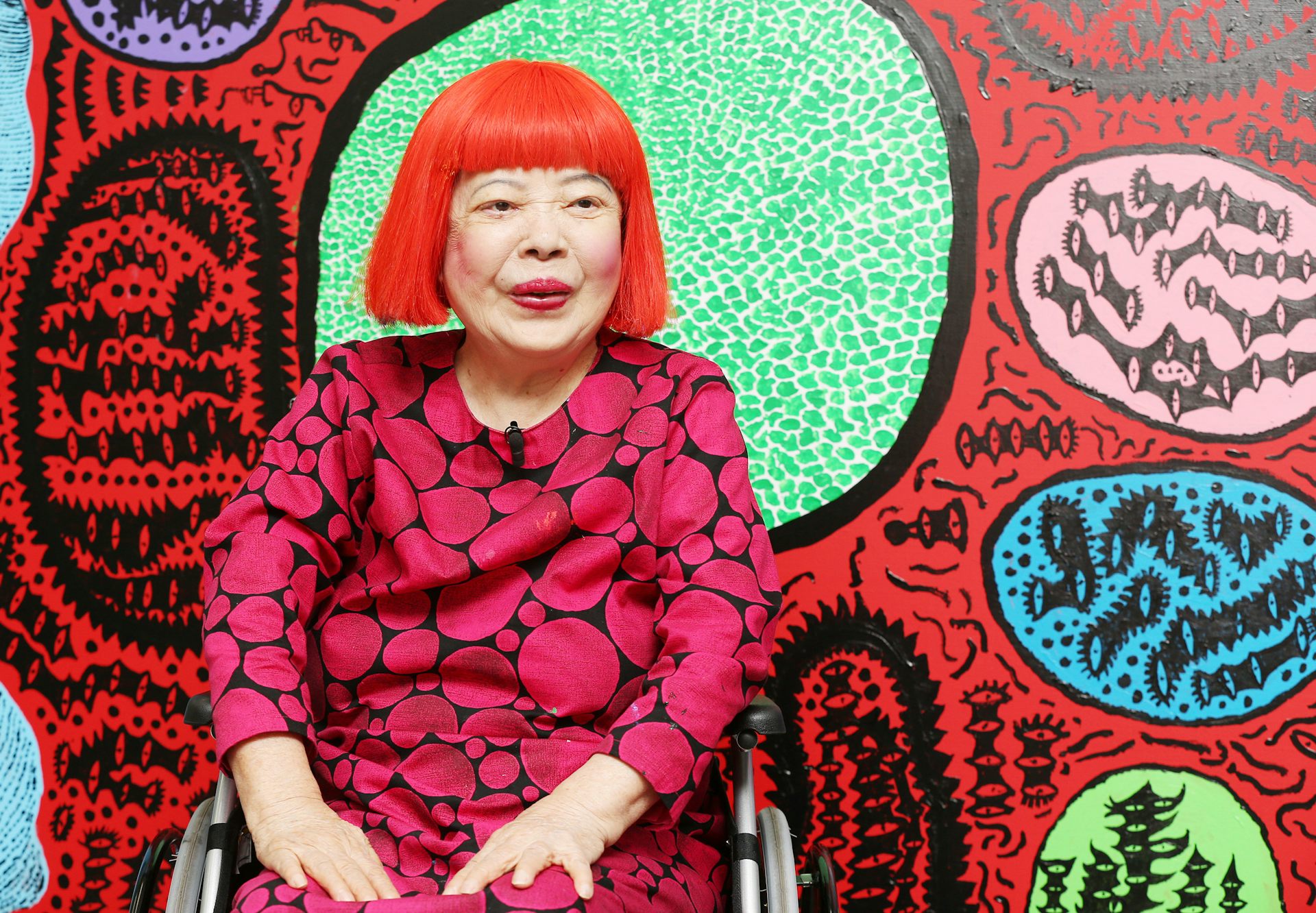 Kusama in a red wig in front of her paintings. 