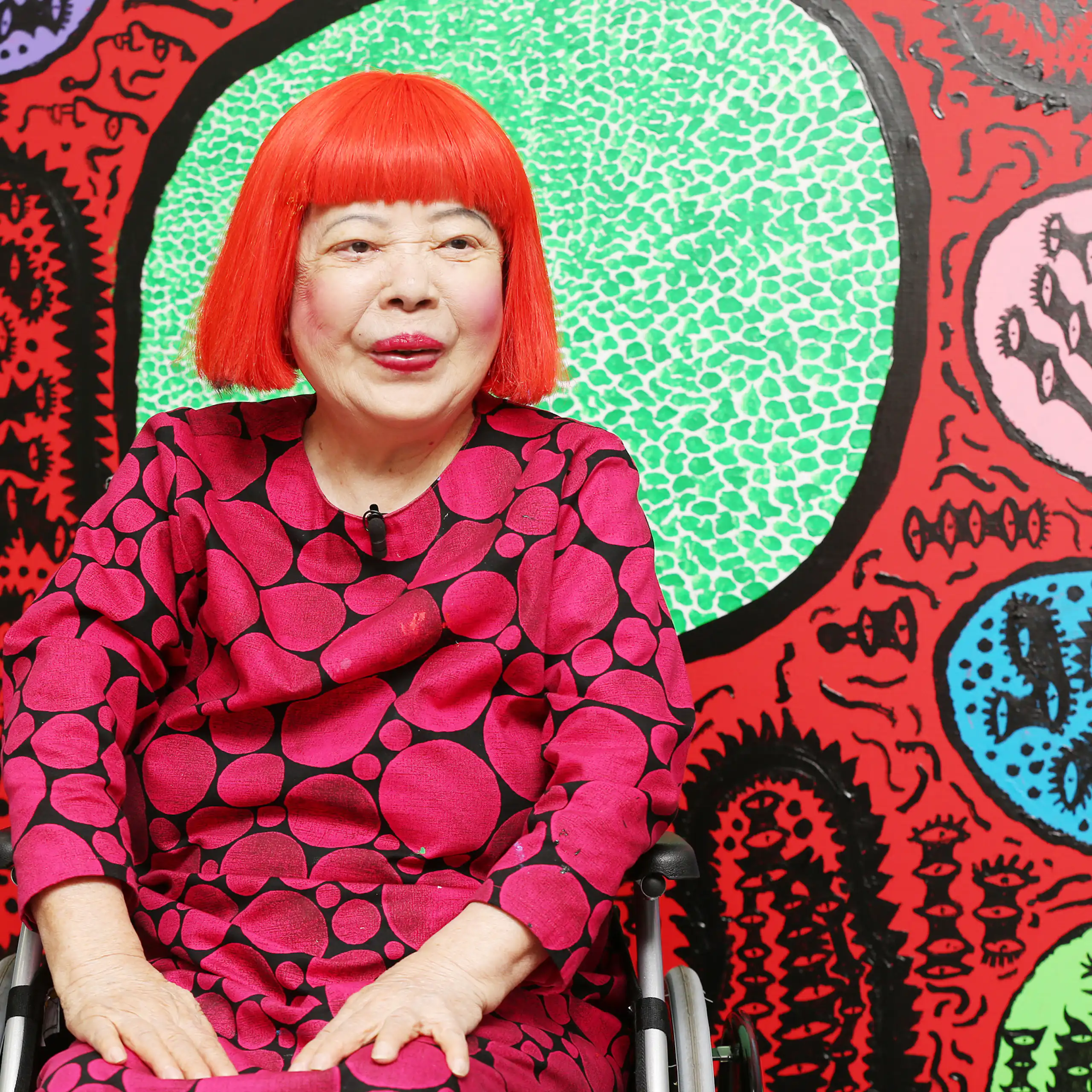 Kusama in a red wig in front of her paintings.