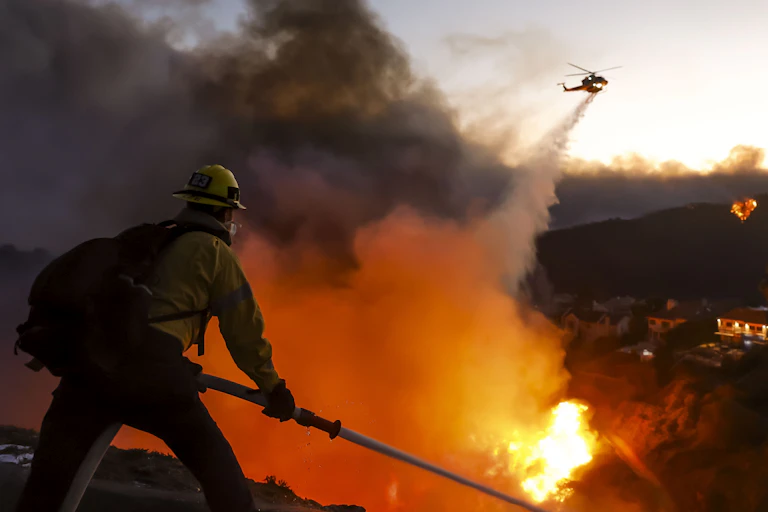 A firefighter battling a blaze with a helicopter nearby.