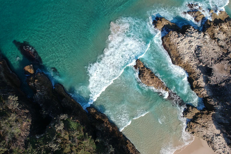 An aerial drone shot of waves lapping at a narrow beach between rock outcroppings.