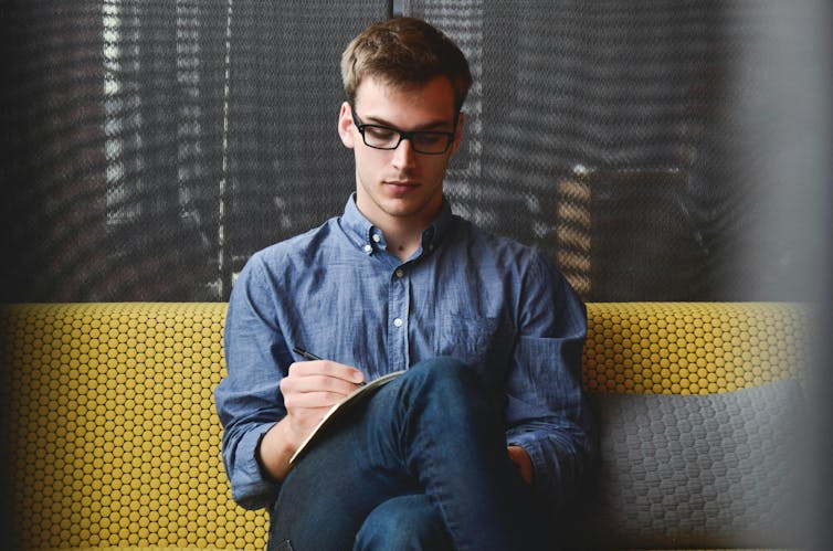 a white man with glasses writing in a notebook