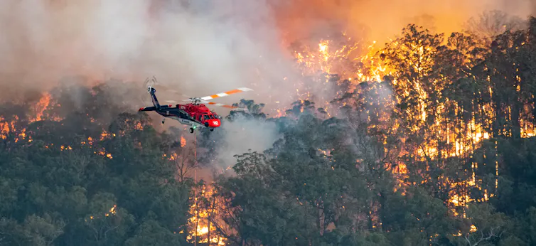 A helicopter flies over a burning forest.
