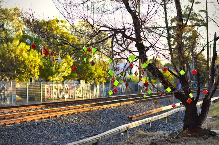 A tree adorned with public art stands to the right of a railway line in north Melbourne.