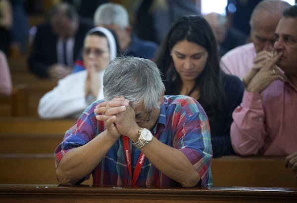 People in pews kneel in prayer, with some holding their clasped hands up toward their faces.