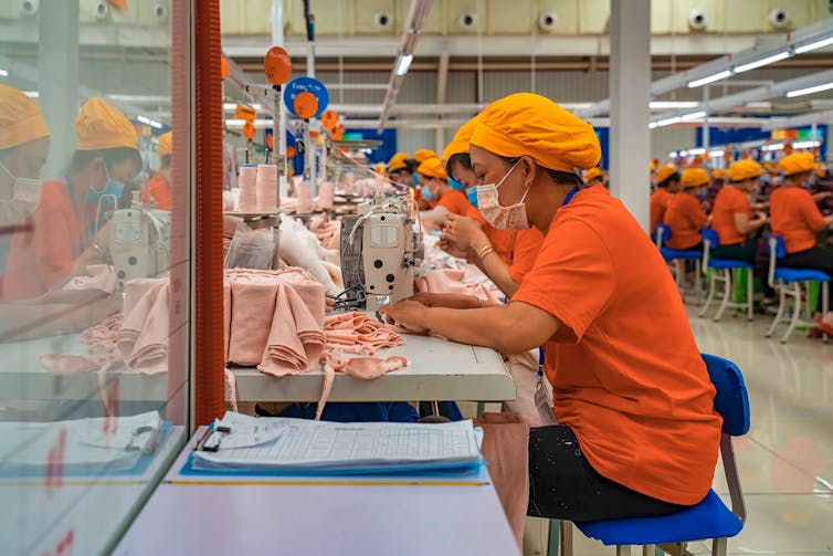 Woman in an orange uniform using a sewing machine on a production line