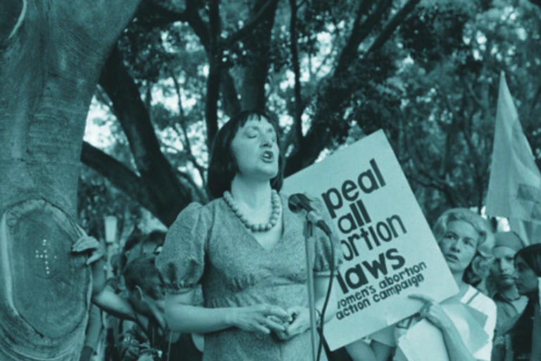 A woman speaks passionately with her eyes closed at a protest rally.