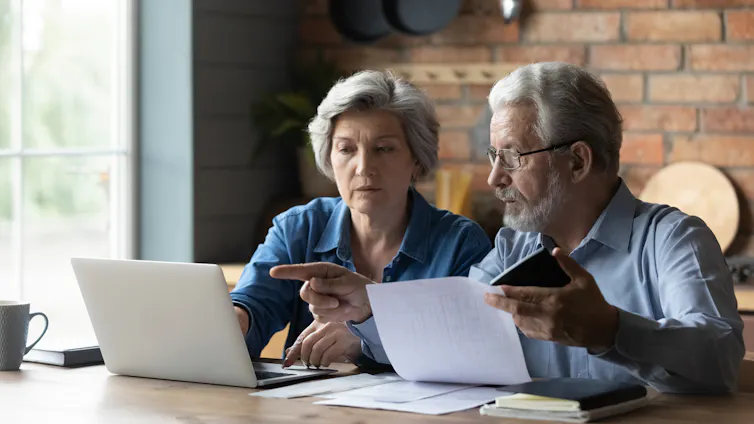 Focused senior husband and wife sit at table