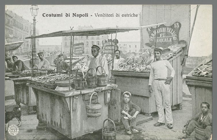 Black and white photograph: sellers at a street stall.