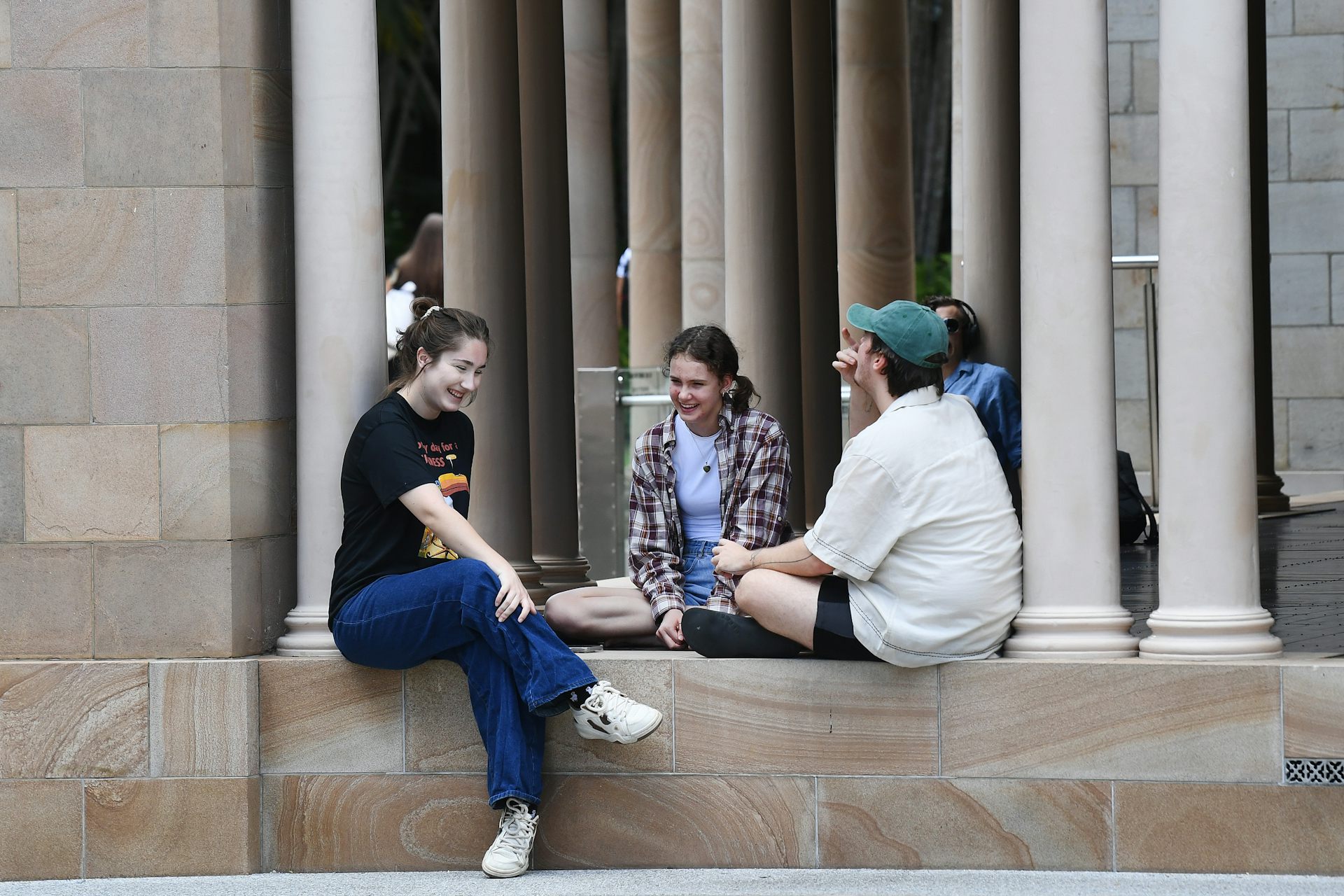 Young people sit and talk on a sandstone ledge.