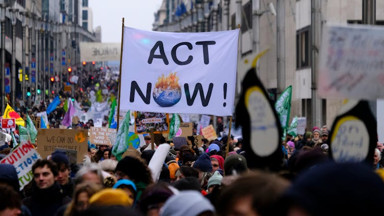 People take part in a climate protest on a city street, holding signs featuring a burning planet Earth.