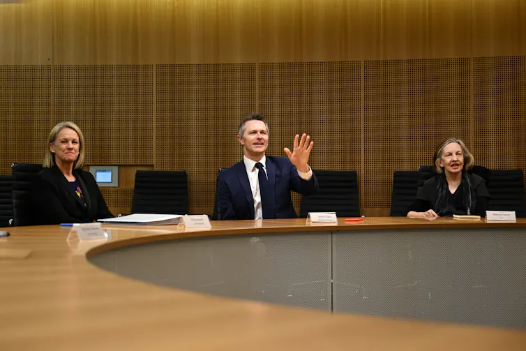 Education Minister Jason Clare sits at a board table with review panel members Fiona Nash and Mary O'Kane.