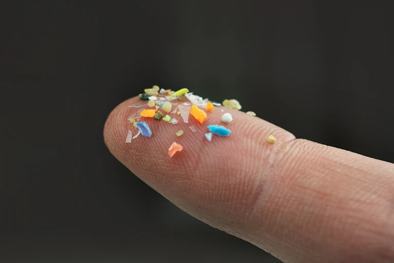 finger holding colourful microplastics, black background