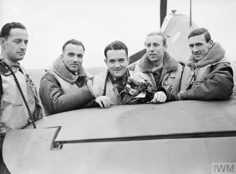 Young polish pilots smile as they pose for a photograph with a fighter aircraft during the second world war.