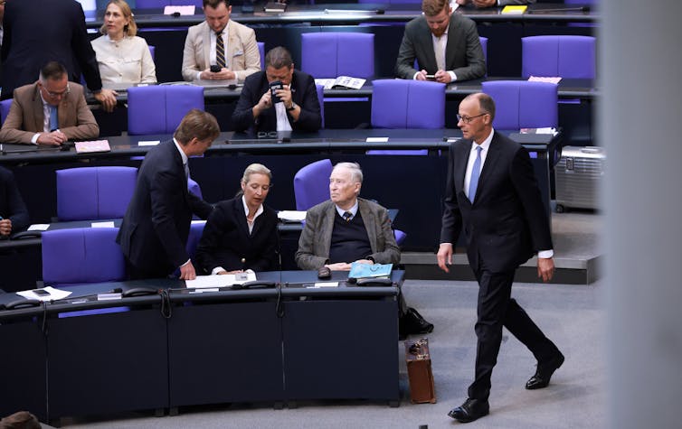 Friedrich Merz walking in front of seated members of the AfD in the German parliament.