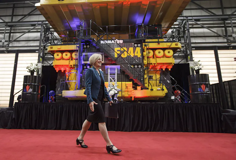 A blond woman walks past a heavy hauler truck at an indoor event.
