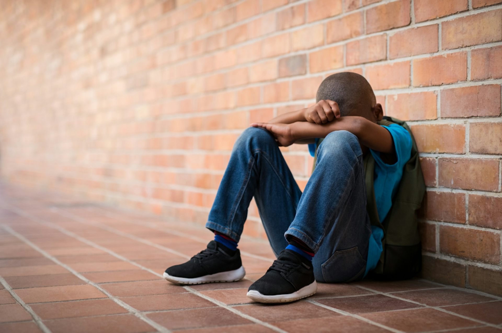 Boy sitting on the floor in a corridor with his head in his hands