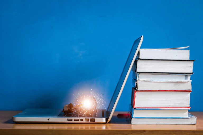 Bright light bulb rests on keyboard of laptop, which is next to a stack of books.