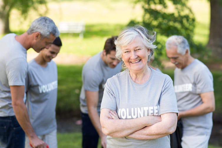 A woman with grey hair looking a the camera, and several people out of focus in background, all wearing Volunteer T-shirts
