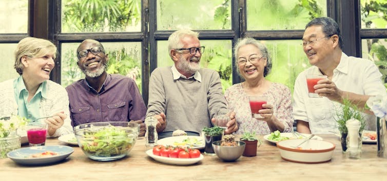 Five older adults sitting at a table with food and drinks