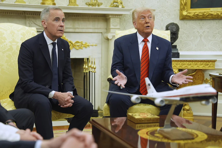 Two men sit side by side, one with short grey hair and an older man with fluffy white-blond hair gesturing with his hands.