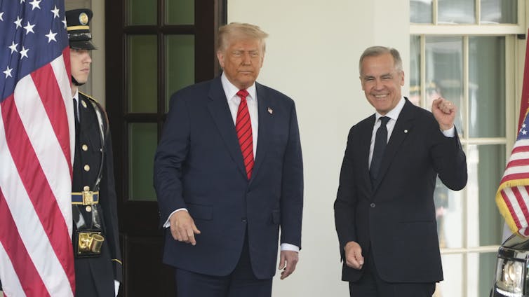 Dos hombres de pie sonrieron a un edificio de piedra blanca con banderas americanas a ambos lados de ellos. Un hombre es un corpulente con un cabello rubio blanco y esponjoso. Otro tiene un cabello gris corto y su puño se eleva.