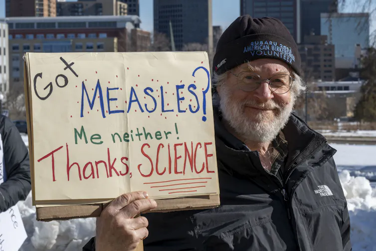 Man holding sign saying, 'Got measles? Me neither! Thanks Science'