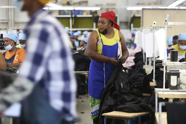A woman in a smock holds a pair of sewing scissors as she works on a garment