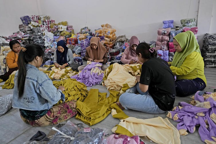 Las mujeres se sientan en clasificar la tierra a través de montones de ropa