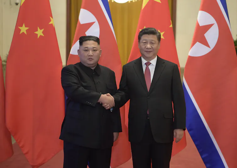 Two men shake hands in front of flags.