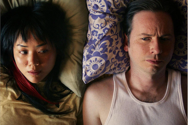 A woman and man staring straight ahead, lying against pillows.