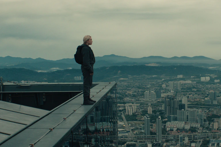 Film still: Florence Pugh stands on the edge of a roof, overlooking a city.