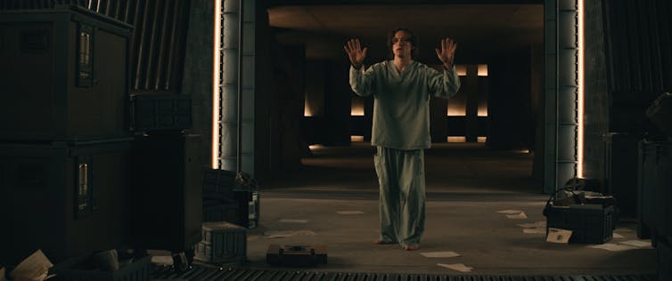 Film still: Bob in pajamas holds his hands up.