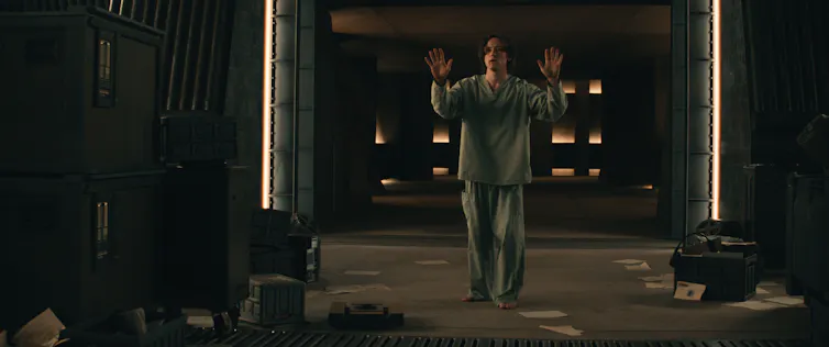 Film still: Bob in pajamas holds his hands up.