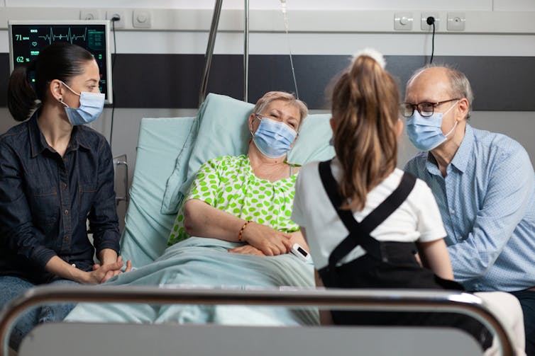 Men, woman and child met with a sick old woman in the hospital, wearing masks