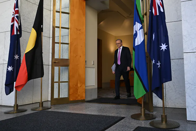 Prime Minister Anthony Albanese exiting Parliament House framed by four flags