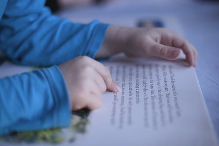Child's hands following words in a book while reading