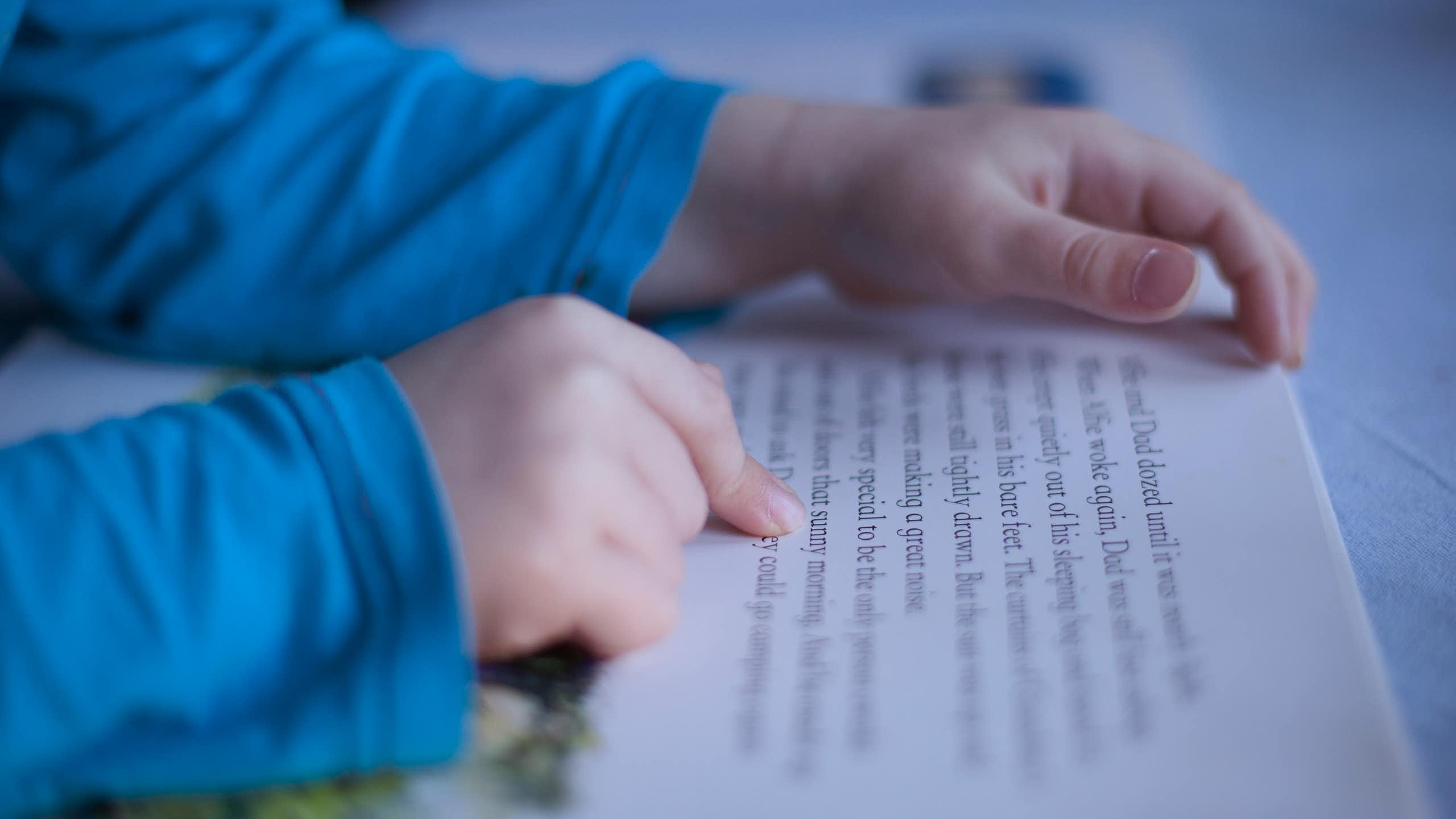 Child's hands following words in a book while reading