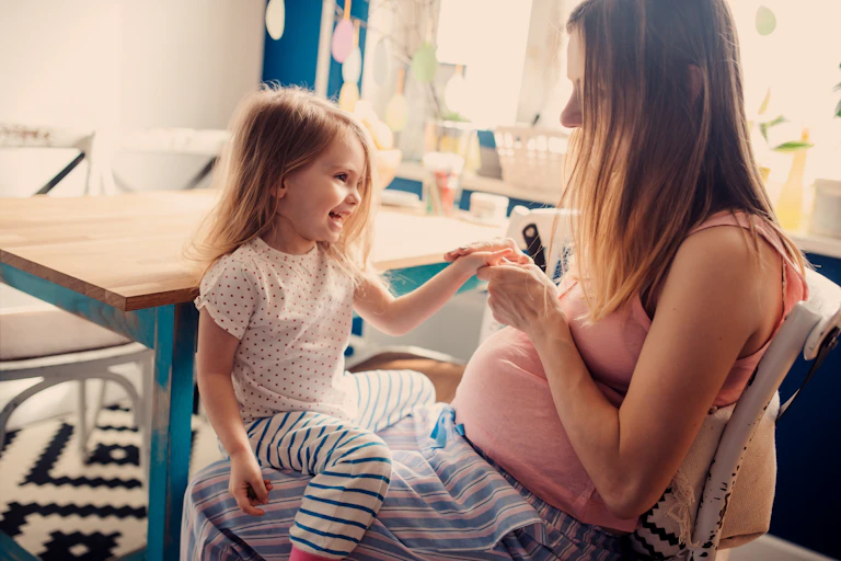 A pregnant woman with a young smiling girl on her lap.