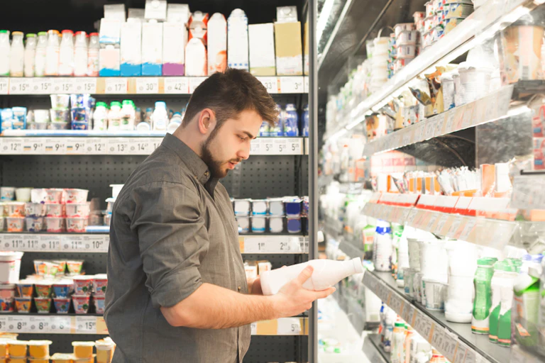 Man standing in front of supermarket milk cabinet, reading label on milk bottle