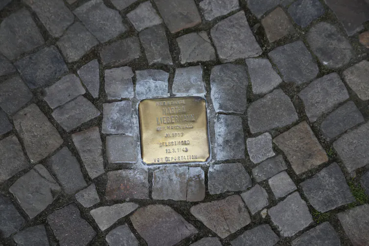 A gold stolperstein set into a cobbled street.